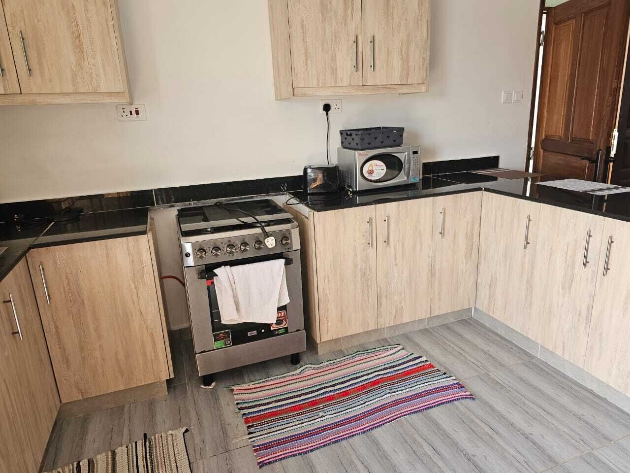 A kitchen with wooden cabinets, a gas stove, a microwave, and a striped rug on the floor.