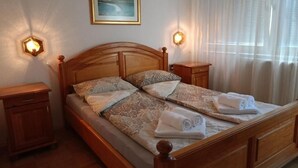 Ein Doppelbett mit Holz Kopfteil, zwei Nachttische, ein gerahmtes Bild an der Wand und ein Fenster mit Vorhängen.