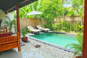 A pool area with two lounge chairs, a wooden bench, and a covered seating area with an umbrella.