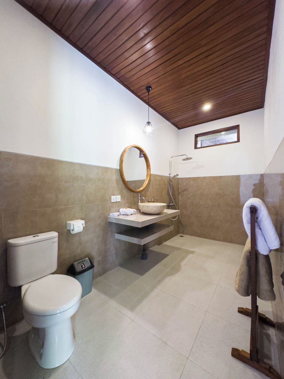 Un baño moderno con techo de madera, un espejo redondo, un lavamanos y un inodoro.