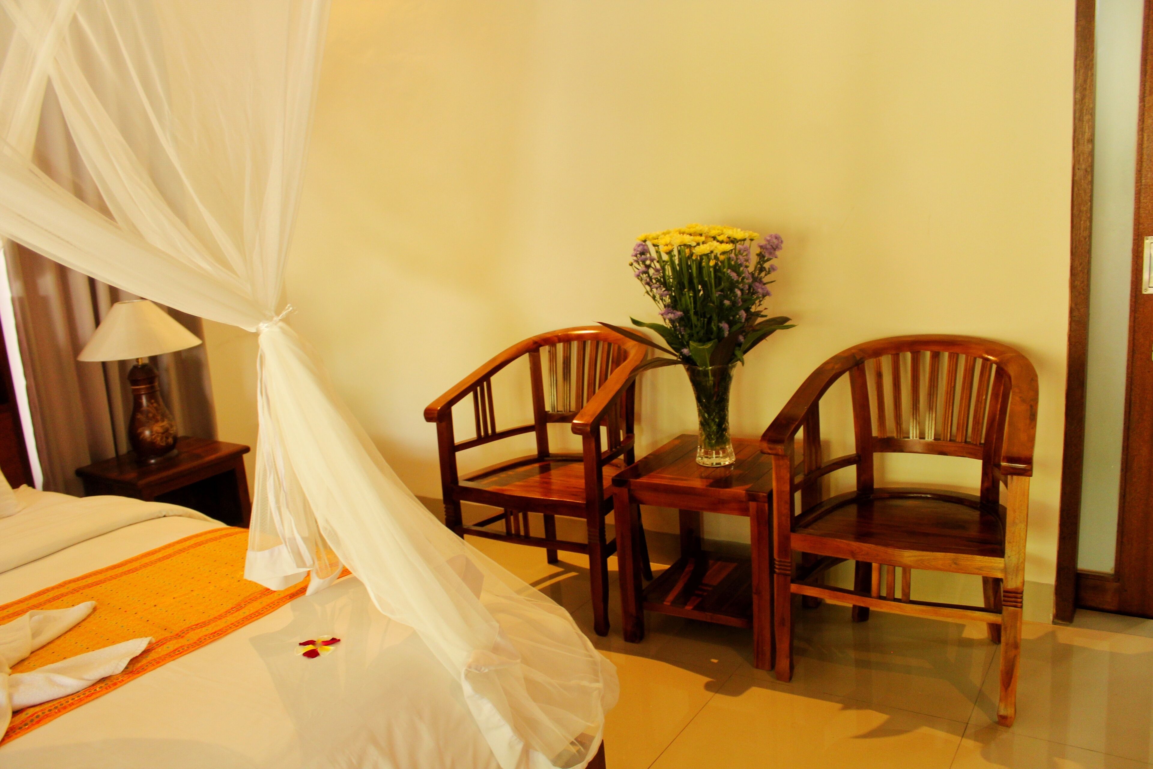Una habitación con una cama, una mesa con sillas y un jarrón con flores.