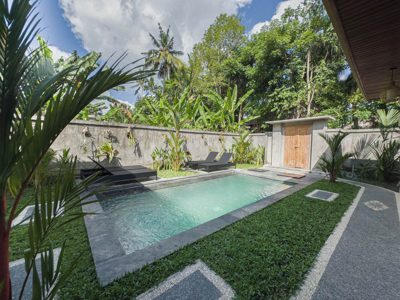 A swimming pool with lounge chairs, surrounded by greenery and a stone wall.