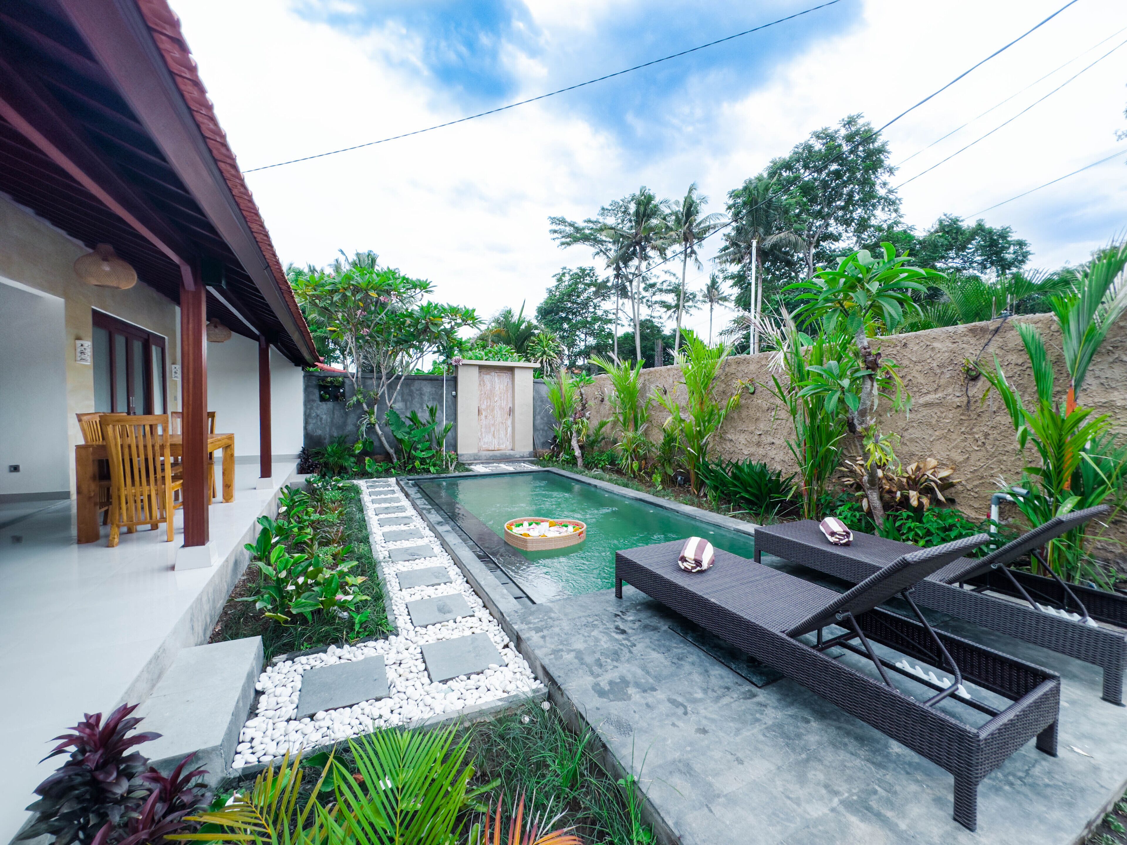 A pool area with lounge chairs, a wooden table, and a stone pathway.