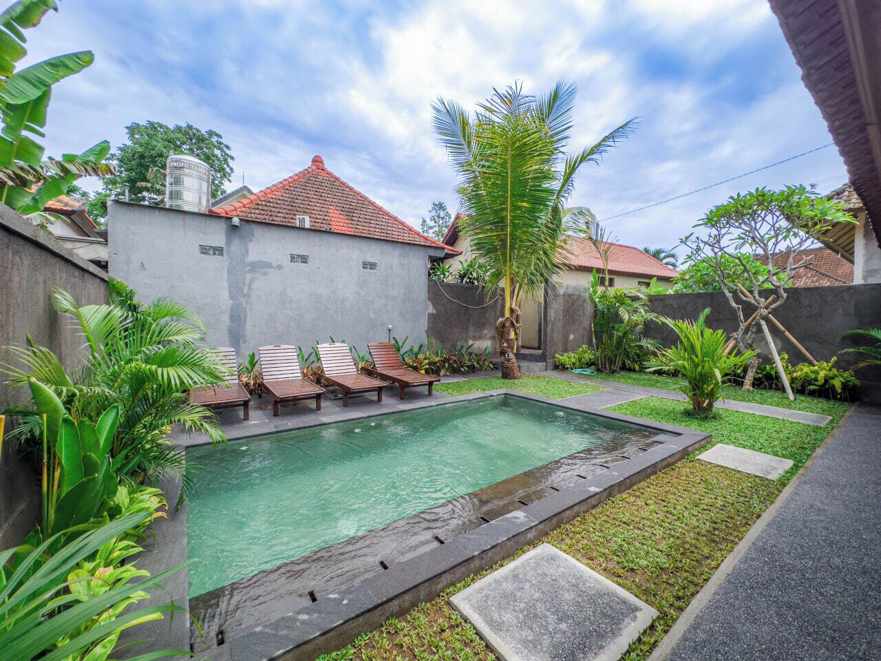 A rectangular swimming pool with a tiled deck, surrounded by a low wall and lush greenery.