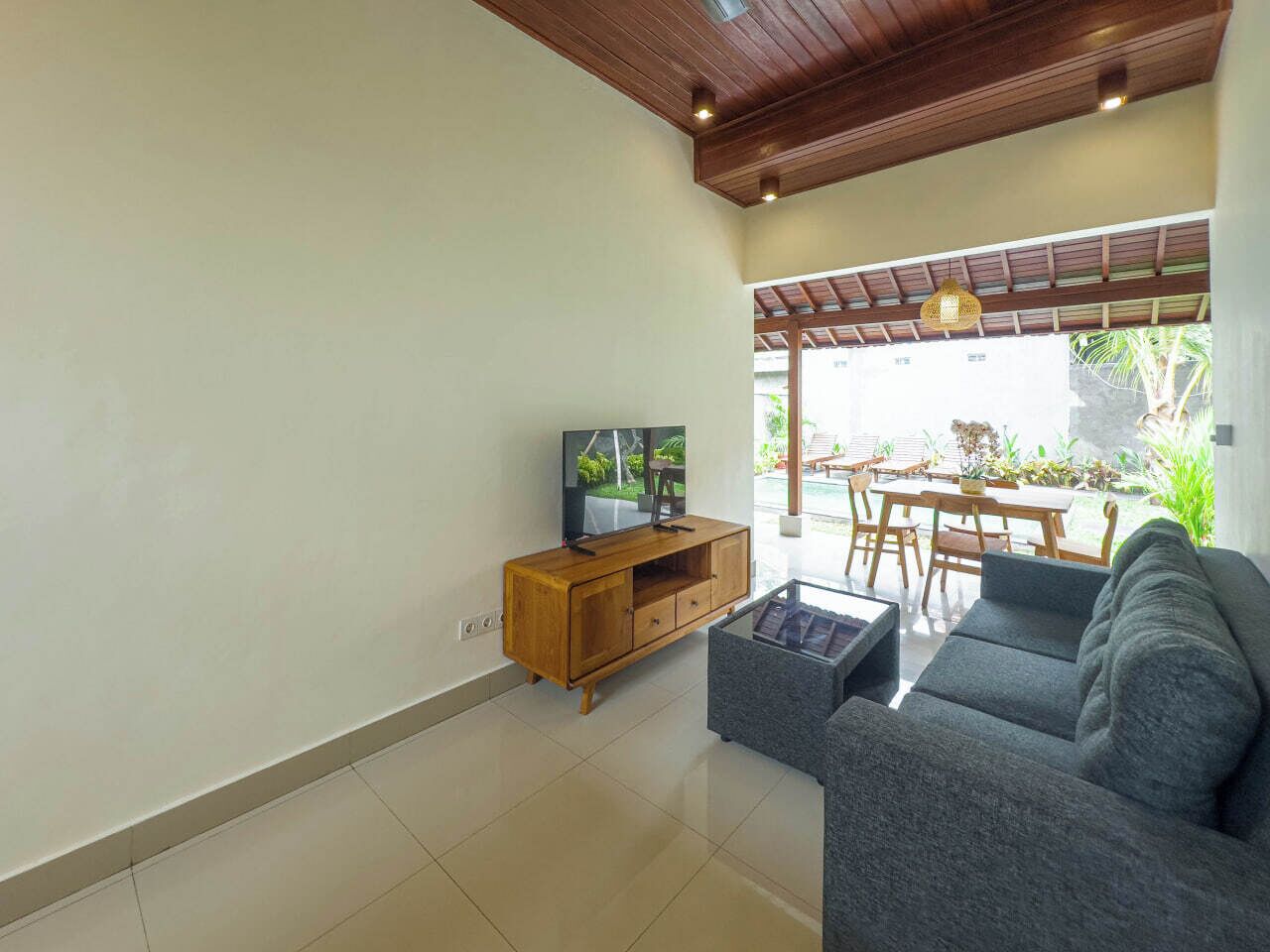 A modern living room with a wooden TV stand, grey sofa, and a glass coffee table.