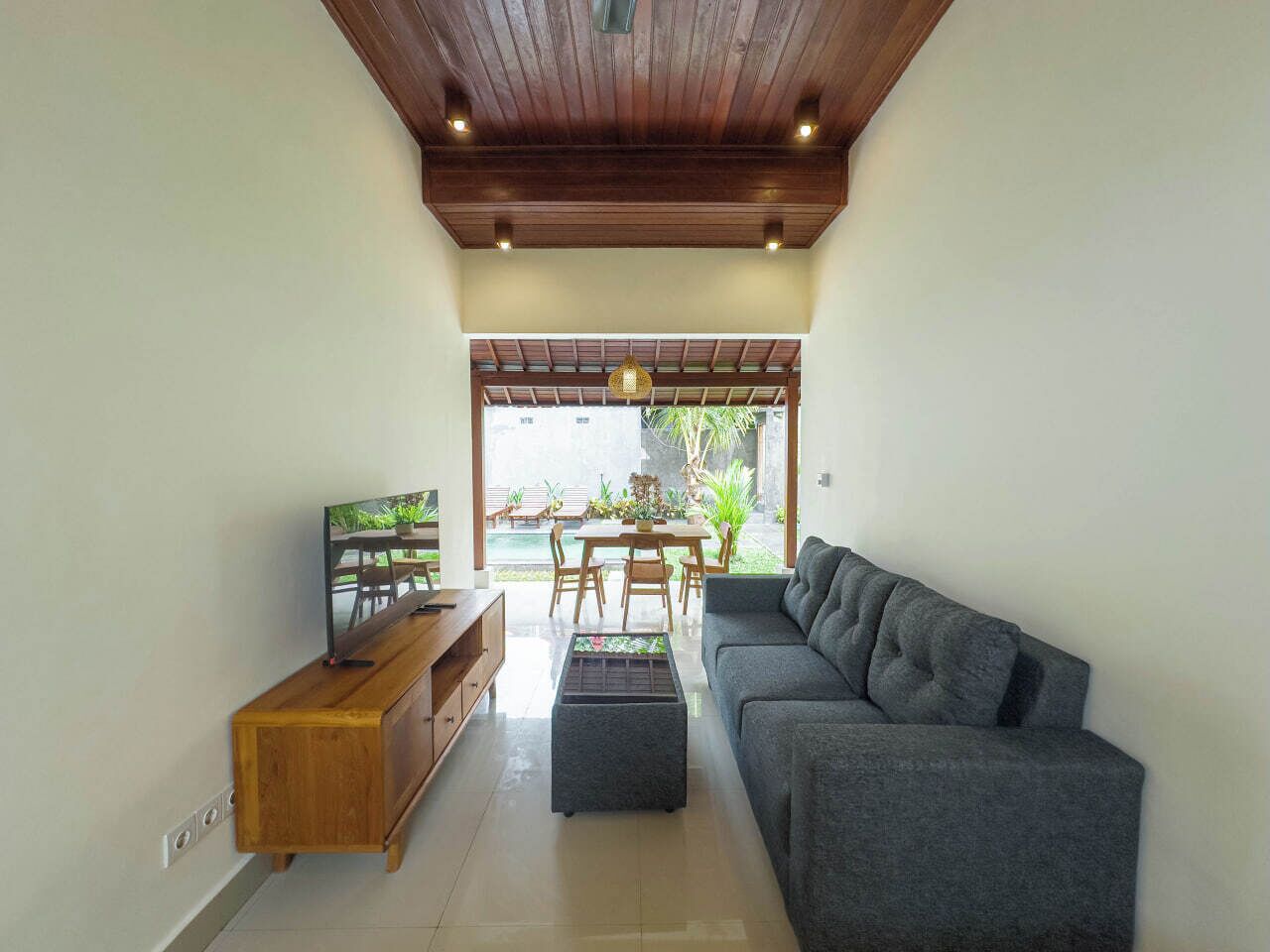 A modern living room with a grey sofa, wooden entertainment unit, and a dining area with a table and chairs.