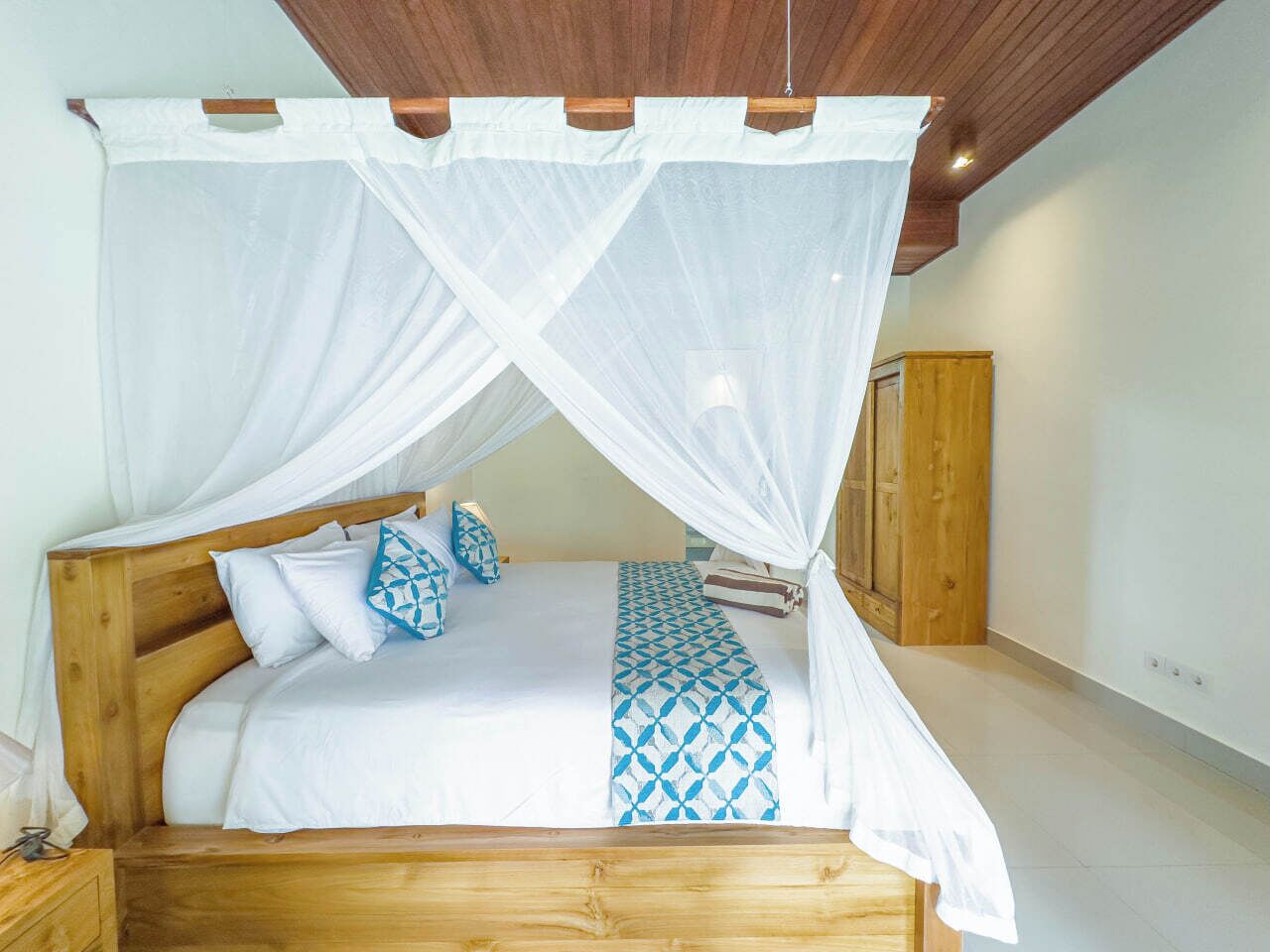 A bed with a wooden frame, white bedding, and a blue patterned throw.