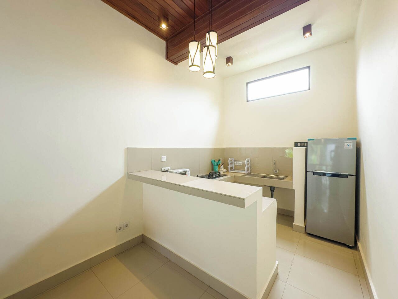 A compact kitchen with a white countertop, a stainless steel refrigerator, and a window providing natural light.