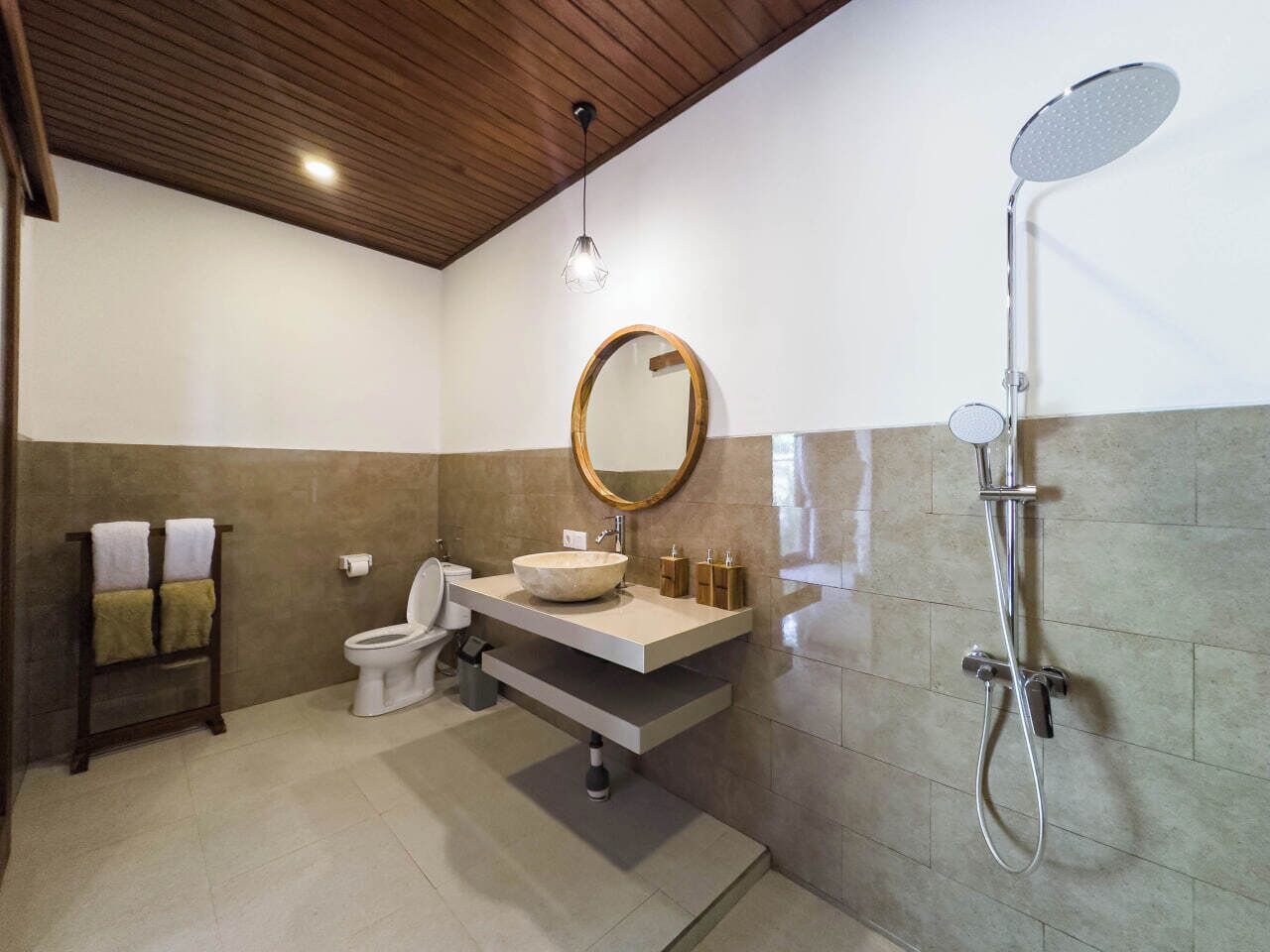 Uma casa de banho moderna com teto de madeira, sanita independente, lavatório com espelho grande e chuveiro.