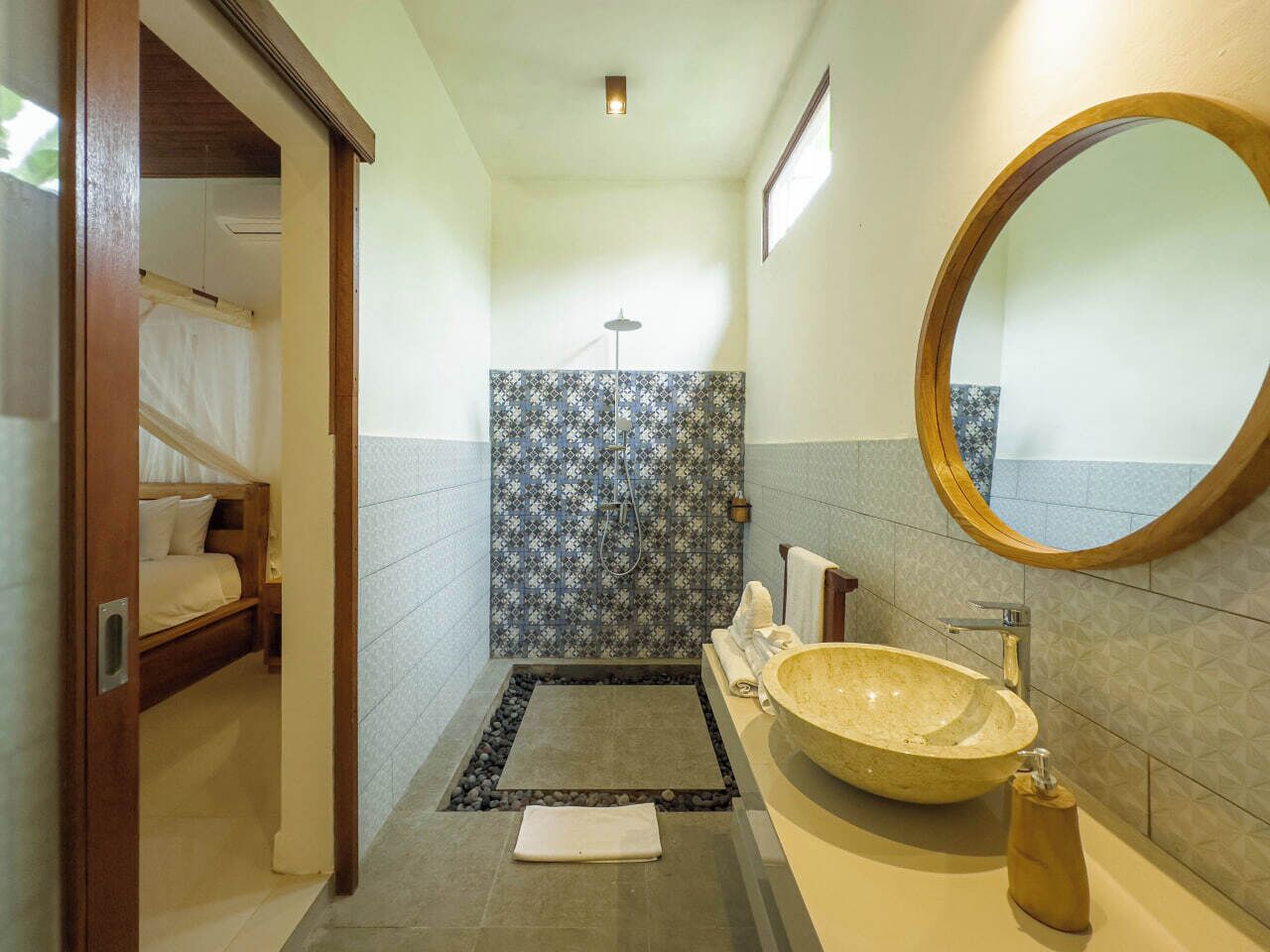 Casa de banho com uma pia grande, chuveiro e uma cama no quarto vizinho.