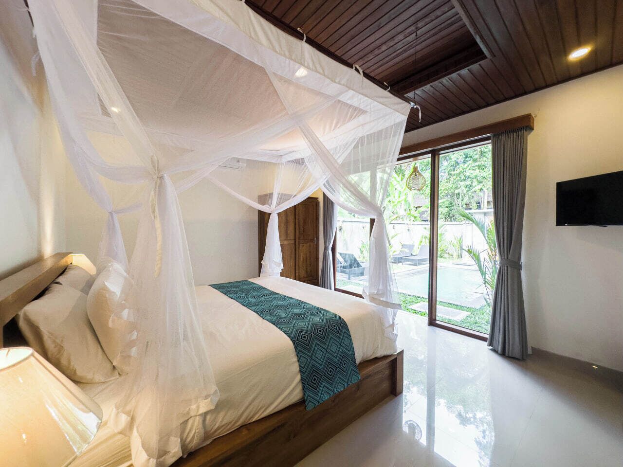 A bedroom with a canopy bed, a large window, and a flat-screen TV on the wall.