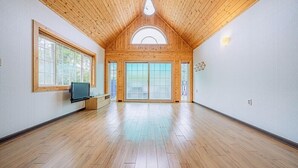 Una habitación amplia con suelo de madera, televisor y ventanas grandes.