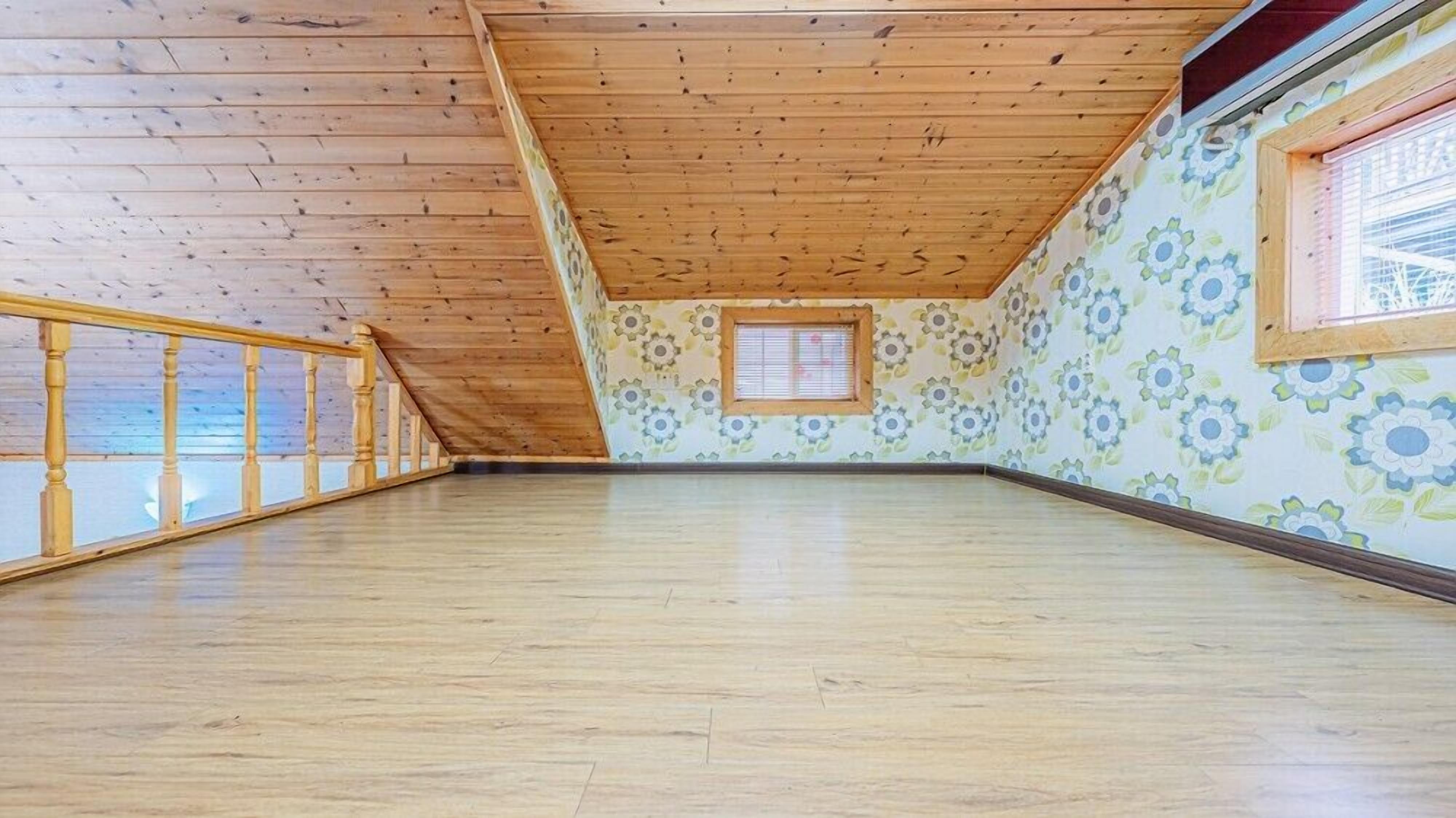 A spacious attic room with wooden beams, a wooden railing, and a floral-patterned wall.
