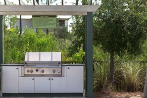 An outdoor grill with a sign detailing grill rules, surrounded by greenery.