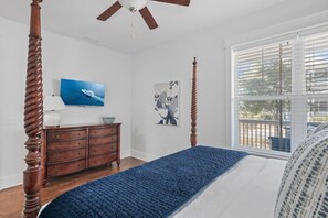 A bedroom with a four-poster bed, a wooden dresser, a ceiling fan, and artwork on the walls.