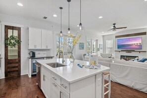 A modern kitchen with white cabinetry, a central island, pendant lighting, and a television mounted above the island.