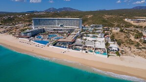 Hotel a la costa amb diverses piscines, una platja i un paisatge de muntanyes al fons.