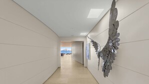 Un passadís amb una decoració mural amb forma d'ala, vista al mar a través d'una porta oberta i un terra emplastrat.