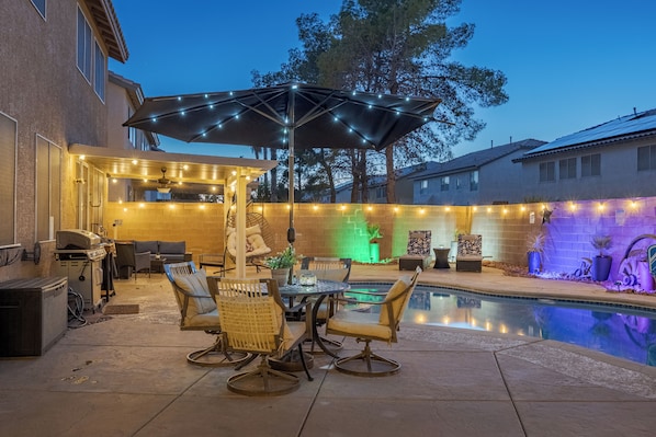 An outdoor patio with a pool, outdoor furniture, and string lights.