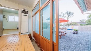 Une pièce dotée d’un plancher en bois, d’une porte-fenêtre coulissante donnant sur un espace extérieur avec une table et des chaises, et d’un petit climatiseur.