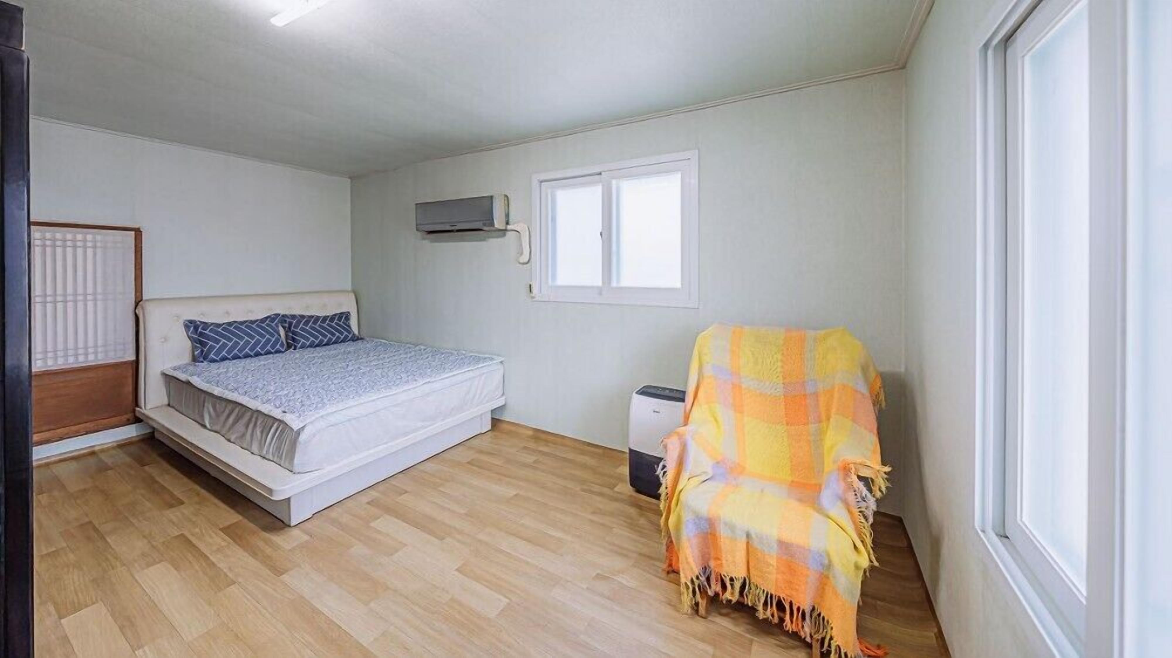 Ein Schlafzimmer mit einem Bett, einem Fenster, einem Heizkörper und einem Sessel mit einer Decke.