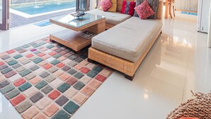 A modern living room with a glass door leading to a pool, a dining area, and a kitchen. - Kakul Villa F by Supala (Ubud)