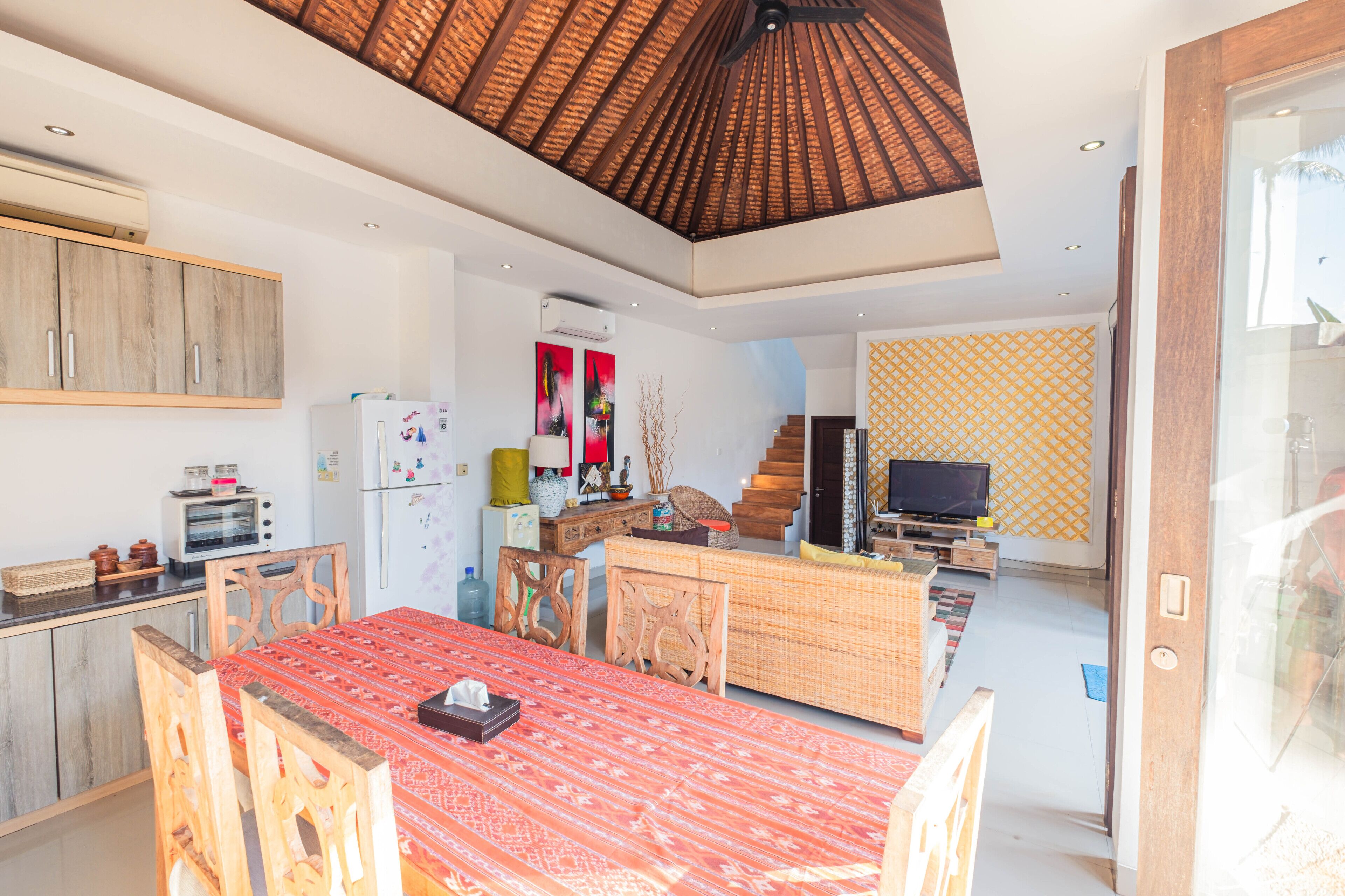 Una cocina moderna con armarios de madera, un comedor con mantel estampado rojo y un televisor en la sala.