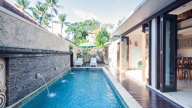 A swimming pool with two lounge chairs, a stone wall, and a wooden deck. - Kakul Villa F by Supala (Ubud)