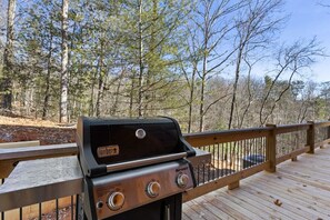 Una parrilla Spirit sobre una terraza de madera con barandal de metal, rodeada de árboles.