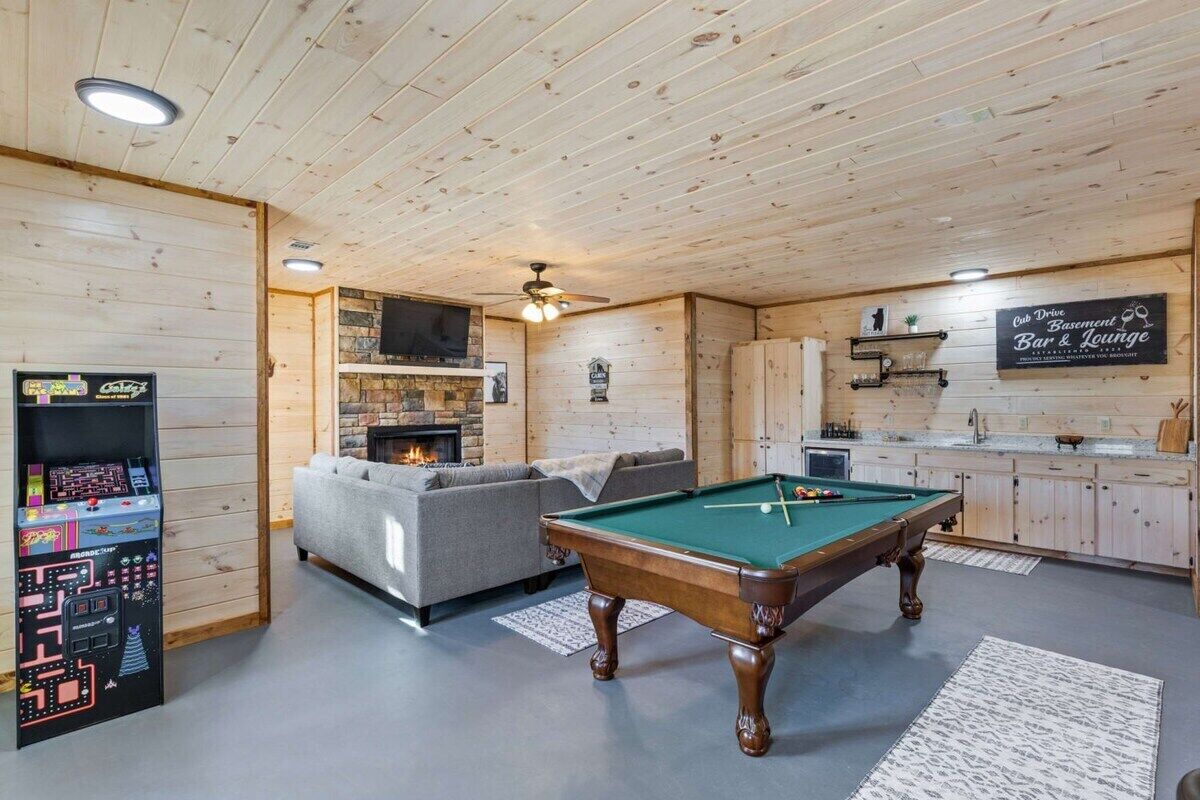Um quarto com painéis de madeira, mesa de bilhar, sofá, lareira e espaço de bar.