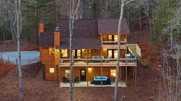 A two-story log cabin with a balcony, a covered porch, and a hot tub.