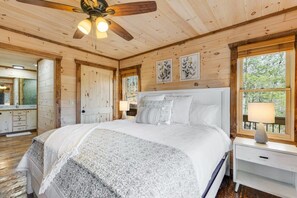 Un dormitorio de cabaña de madera con cama, mesita de noche y ventilador de techo.