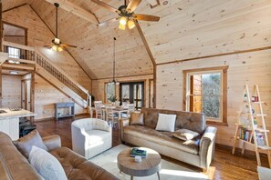 Interior espacioso de una cabaña de madera con un entrepiso con habitación, un comedor y una sala de estar amoblada con sofás de cuero y una mesa de centro.