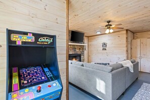 A room with a Pac-Man arcade game, a fireplace, a sofa, and a ceiling fan. - Blue Ridge Mtn Cabin – Hot Tub, Pool Table, Fire Pit (Mineral Bluff)