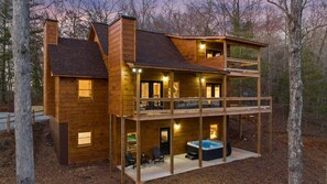 A two-story log cabin with a balcony, a hot tub, and a deck area.