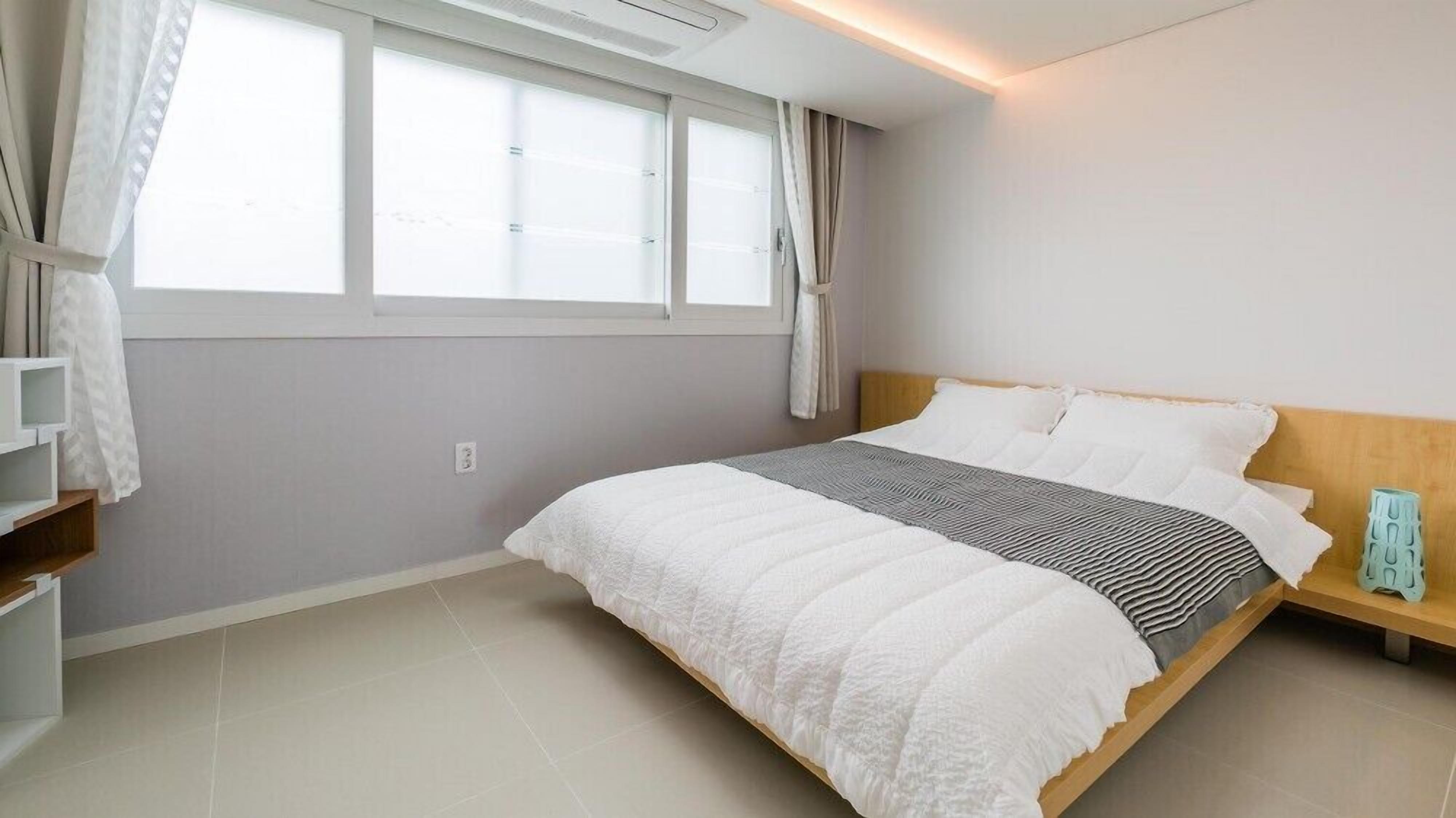 Un dormitorio moderno con una cama grande, una mesita de noche, un armario y una ventana con cortinas.