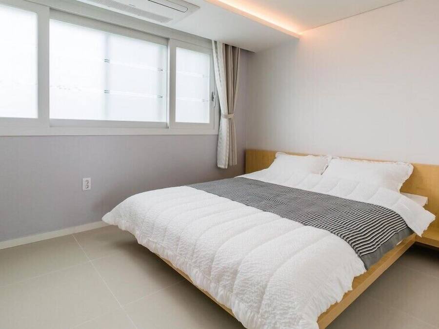 Un dormitorio moderno con una cama grande, una mesita de noche, un armario y una ventana con cortinas.