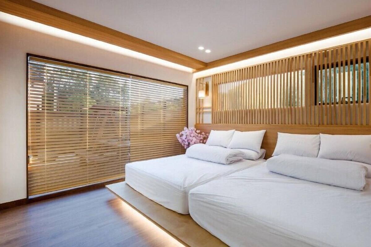 Ein modernes Schlafzimmer mit zwei Betten, Holz-Kopfteilen und einem großen Fenster mit Jalousien.