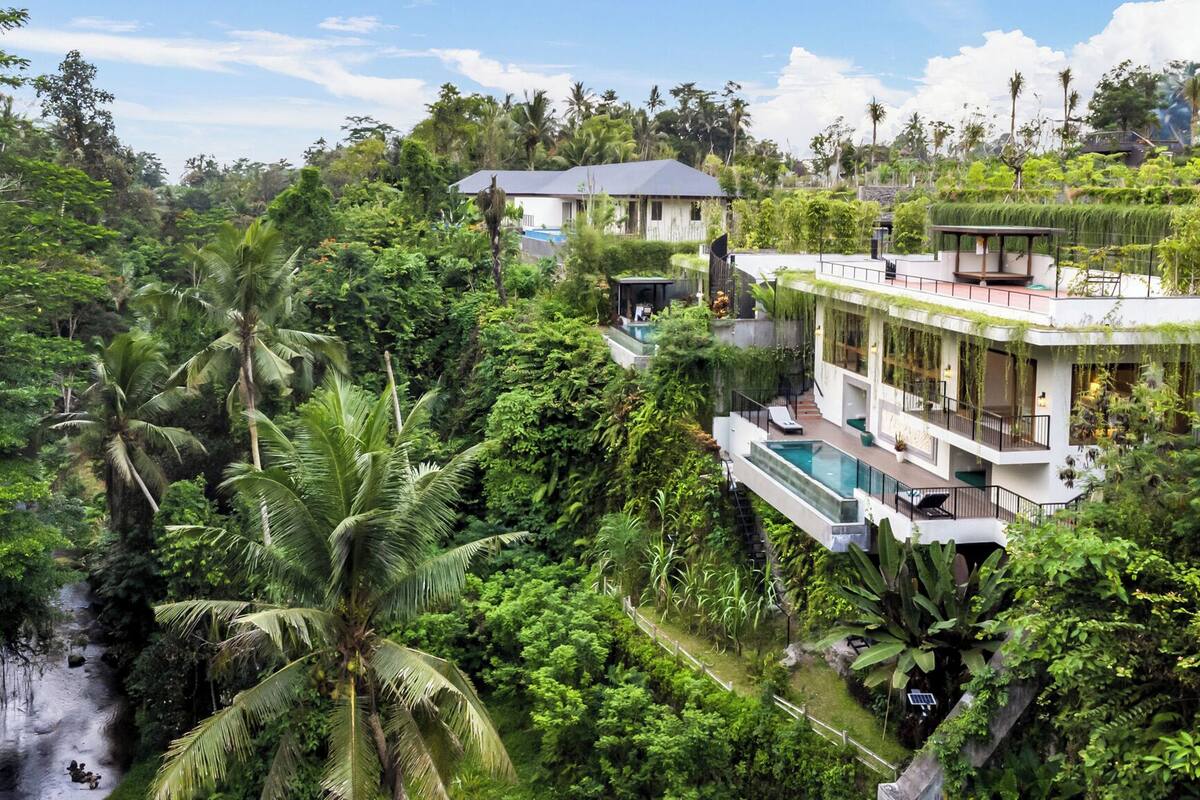 A modern villa with a pool, surrounded by lush tropical vegetation and a waterfall.