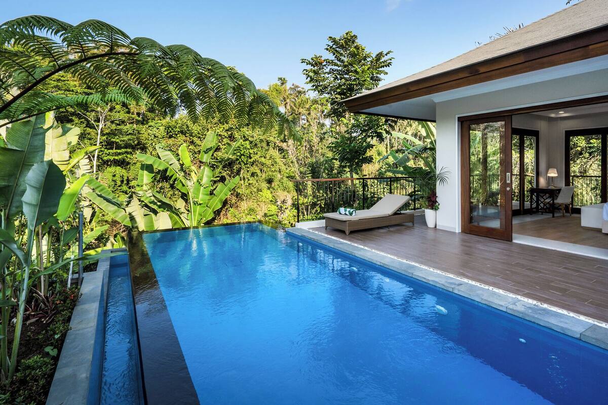 A modern poolside area with a clear blue pool, wooden deck, and lush greenery.