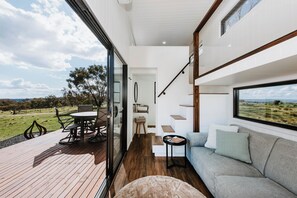 A modern interior with a wooden deck, a grey sofa, and a dining area with chairs and a table.