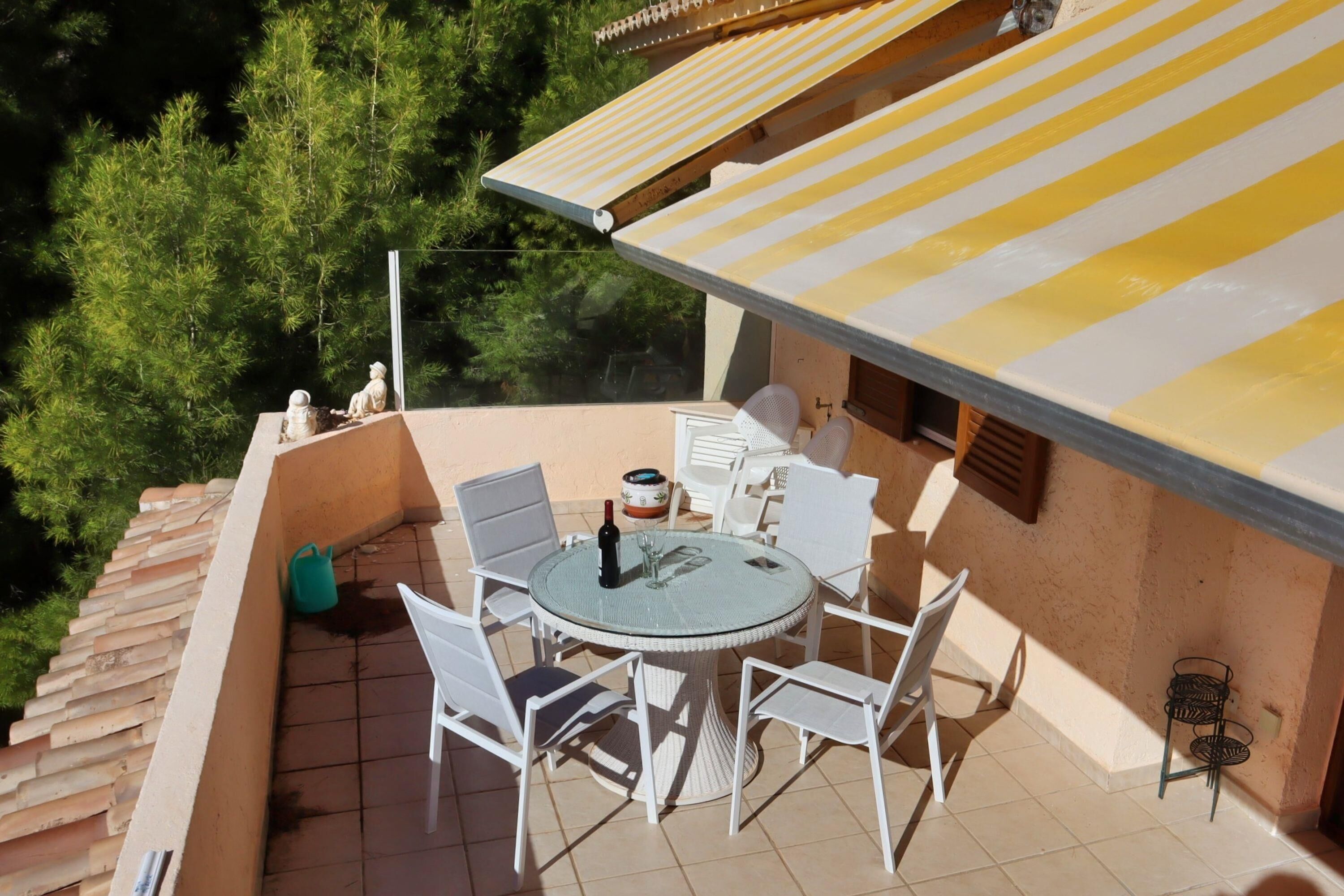 A round table with white chairs on a balcony, a bottle, and a glass on the table.