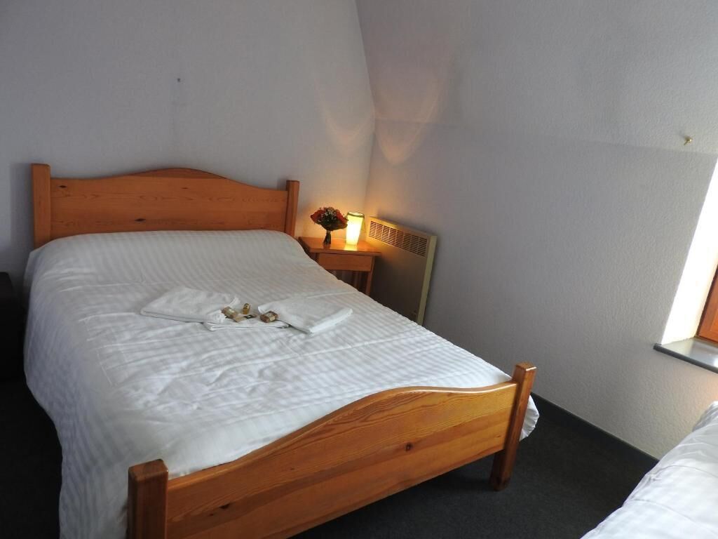 A single bed with a wooden headboard, a bedside table with a lamp, and a window with a view of the outside.