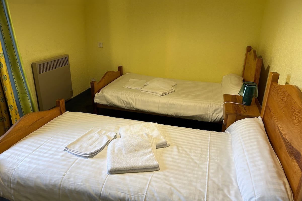 A room with two single beds, each with a wooden headboard, a small bedside table, and a lamp.