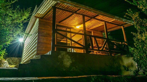 Uma cabana de madeira com varanda, rodeada por árvores.