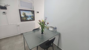 A conference room with a glass table, a black chair, a vase with flowers, a water bottle, and a painting on the wall. - Vu's Home-apartment Junior 40m2 (Prague)