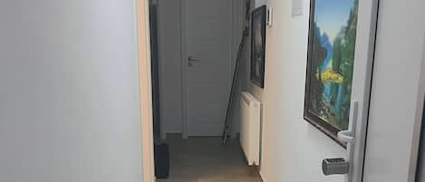 Un pasillo con suelo de baldosas, una puerta con cerradura electrónica y un cuadro en la pared.