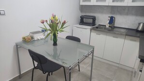 Una cocina moderna con armarios blancos, una mesa de comedor de vidrio, una silla negra, un tostador, un hervidor y un florero con flores.