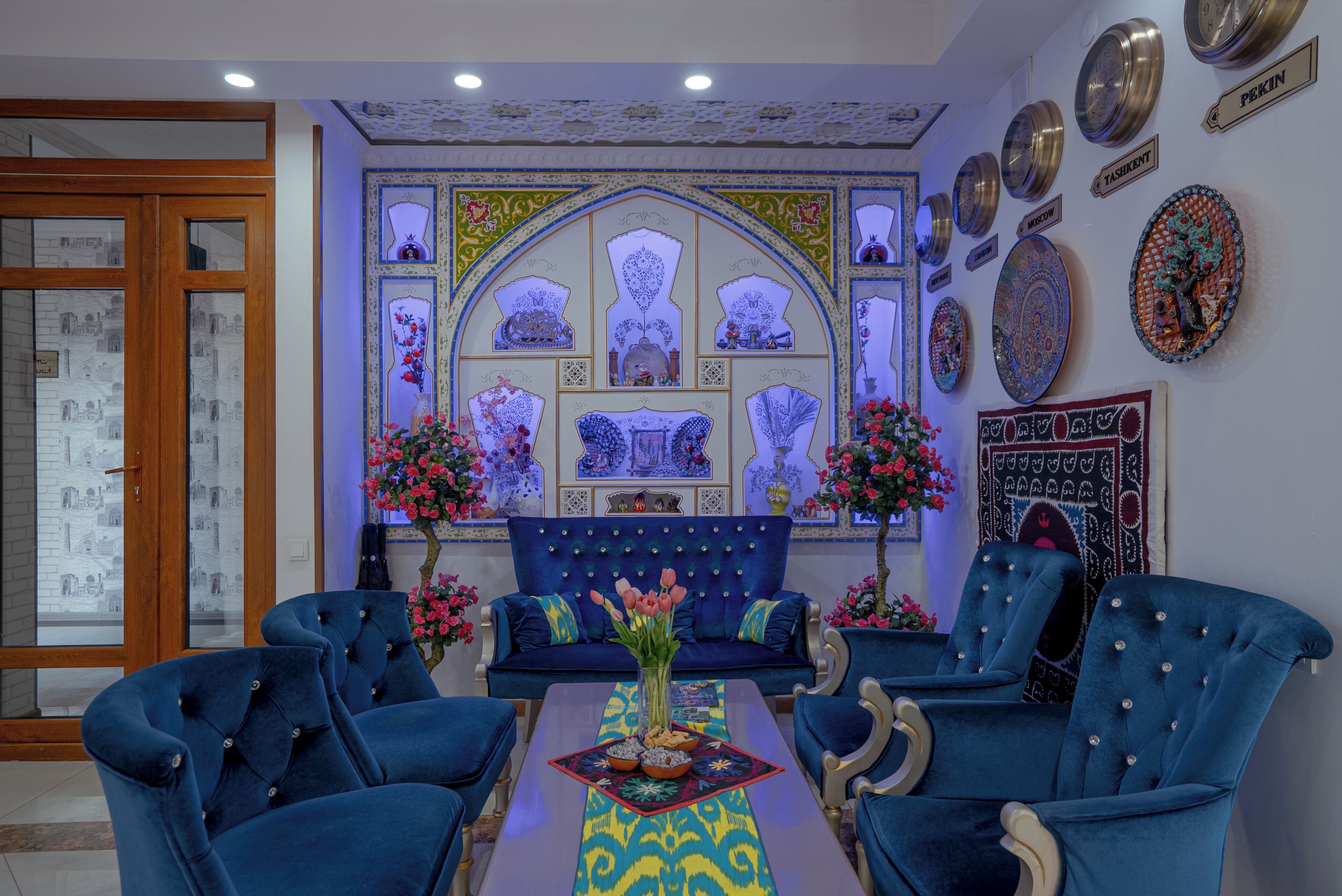 A room with a blue sofa set, a coffee table with a decorative centerpiece, and a wall with various framed artworks.