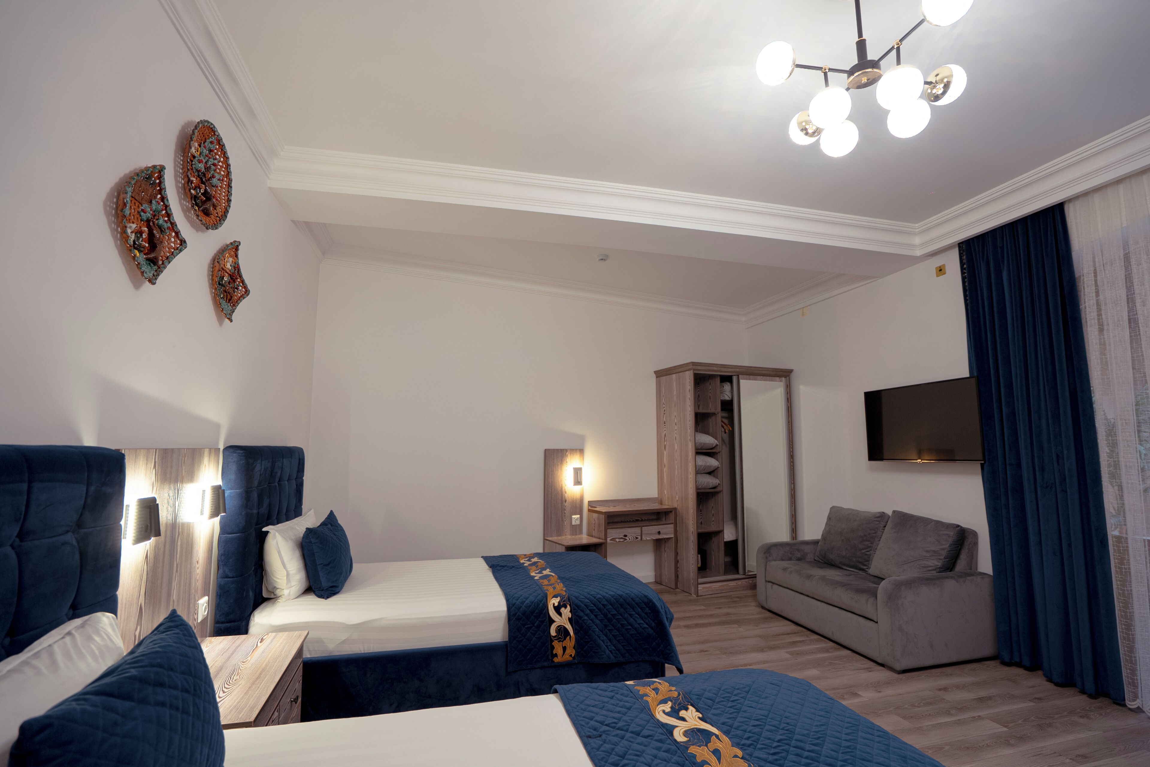 A hotel room with two beds, a desk, a sofa, a wardrobe, and a TV.